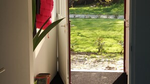Una puerta que da a un jardín con un árbol, una chaqueta roja colgada en la pared y botas en el suelo.