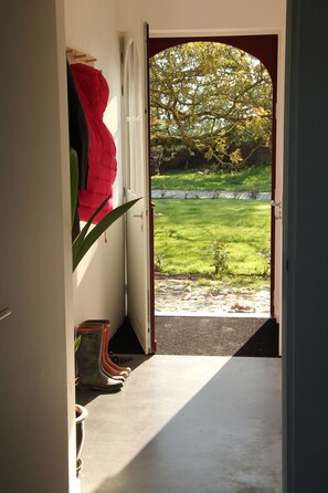 A doorway leading to a garden with a tree, a red jacket hanging on the wall, and boots on the floor. - Renovated house in an old farmhouse 12km from the center of Brussels (Sint-Pieters-Leeuw)