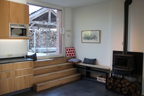 A modern kitchen with wooden cabinetry, a built-in microwave, a window with a view of a wooden deck, and a wood-burning stove. - Renovated house in an old farmhouse 12km from the center of Brussels (Sint-Pieters-Leeuw)