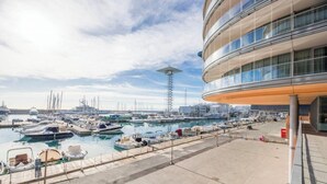 Un puerto deportivo con barcos amarrados, un edificio moderno con grandes ventanales y un cielo despejado.