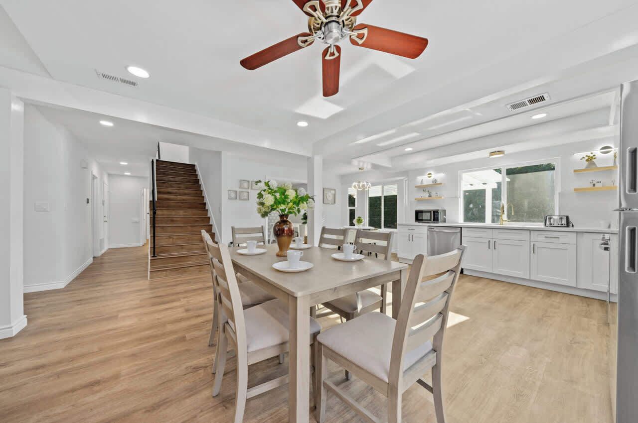 A spacious kitchen with white cabinets, a dining area with a wooden table and chairs, and a staircase leading to another level.