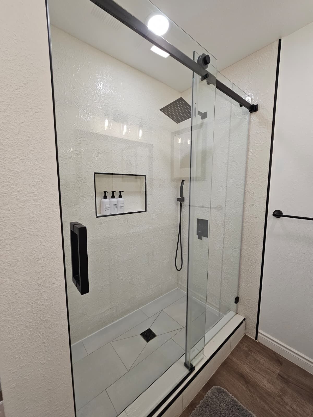 A glass-enclosed shower with a control panel, a framed informational sign, and a wooden floor.