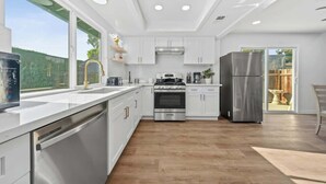 A modern kitchen with white cabinetry, stainless steel appliances, and a large window. - @ Marbella Lane Modern Home w/ Private Backyard (Fullerton)