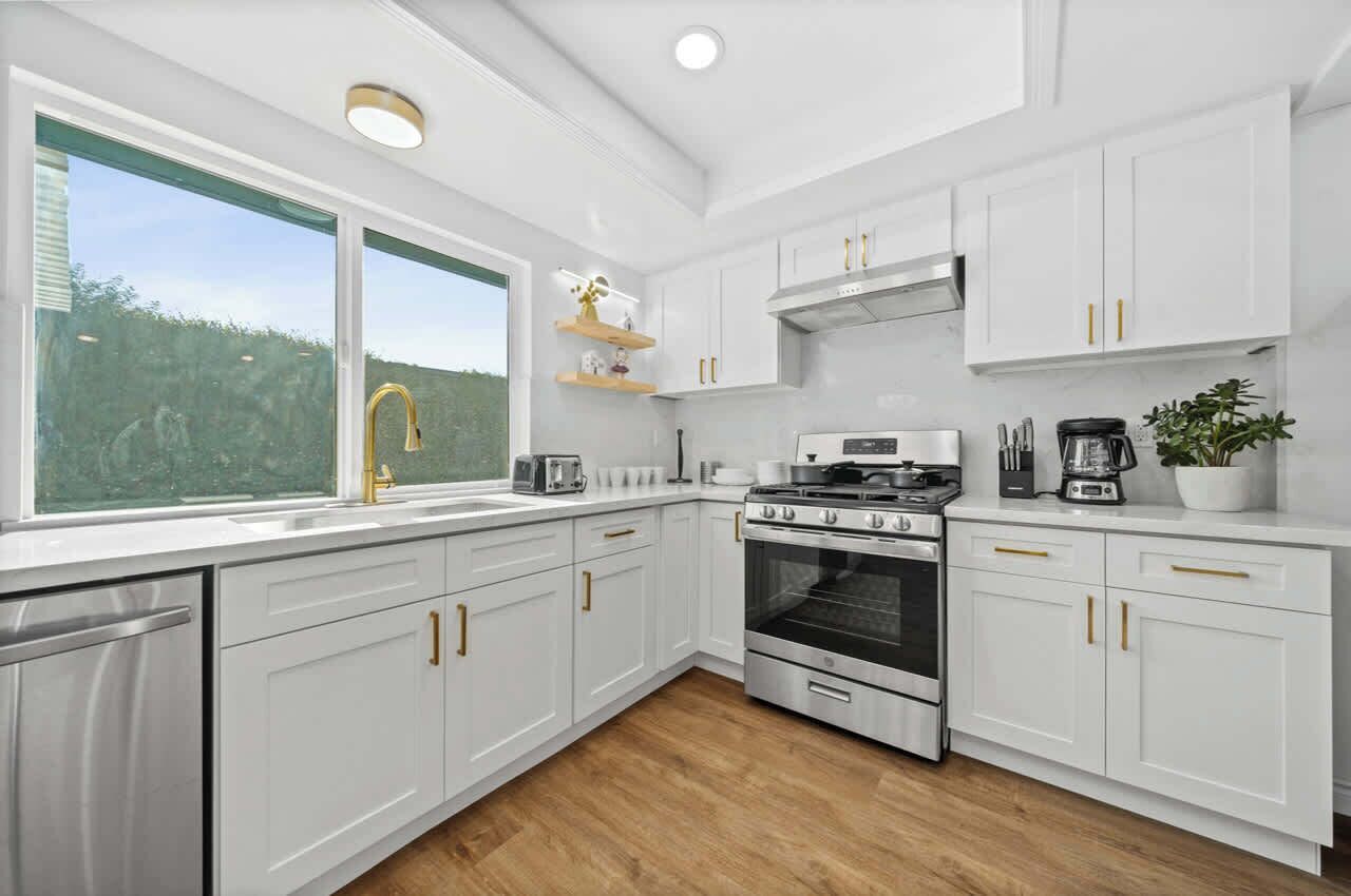 Una cocina moderna con armarios blancos, una estufa de acero inoxidable y una ventana con vistas a zonas verdes.