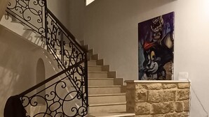 Una escalera con barandillas de metal ornamentadas, un muro de piedra, un cuadro, un sofá y una mesa blanca.
