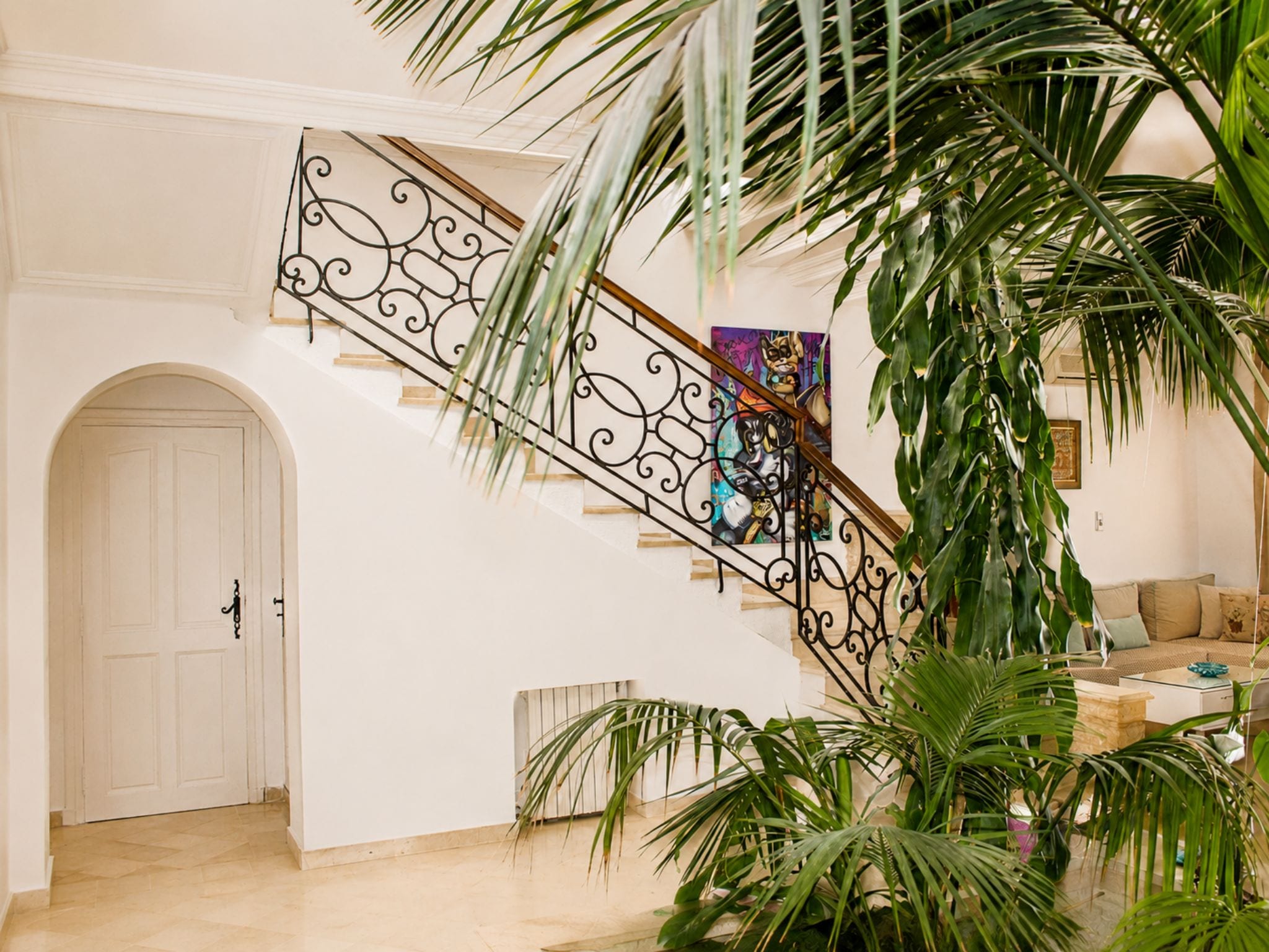 A staircase with ornate metal railings, a white door, and a living room area with a sofa and a coffee table.