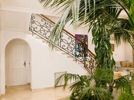 Una escalera con barandillas metálicas ornamentadas, una puerta blanca y un área de sala con un sofá y una mesa de centro.
