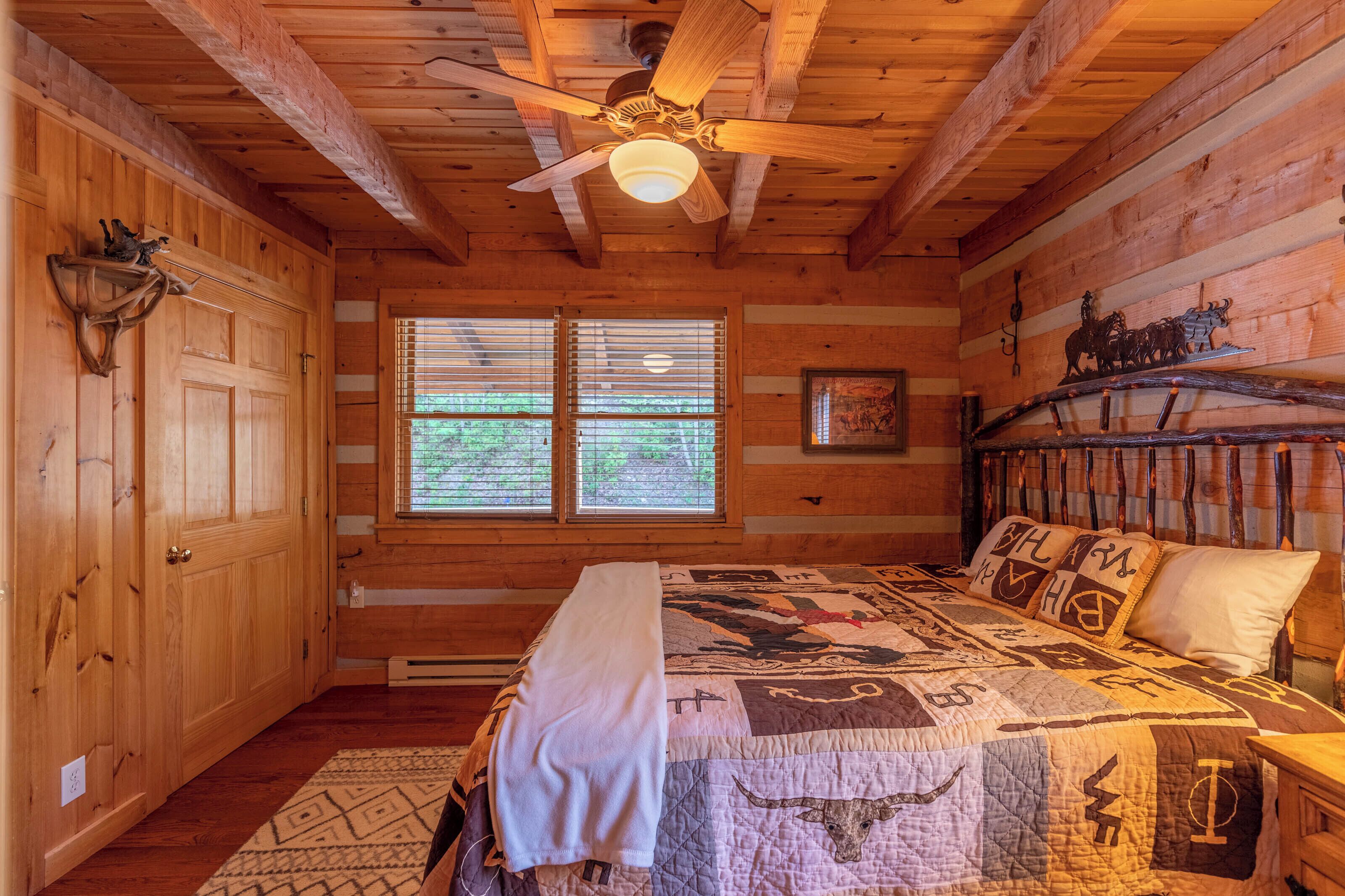 Quarto de cabana de tronco com cama, ventilador de teto, paredes de madeira e janela com persianas.