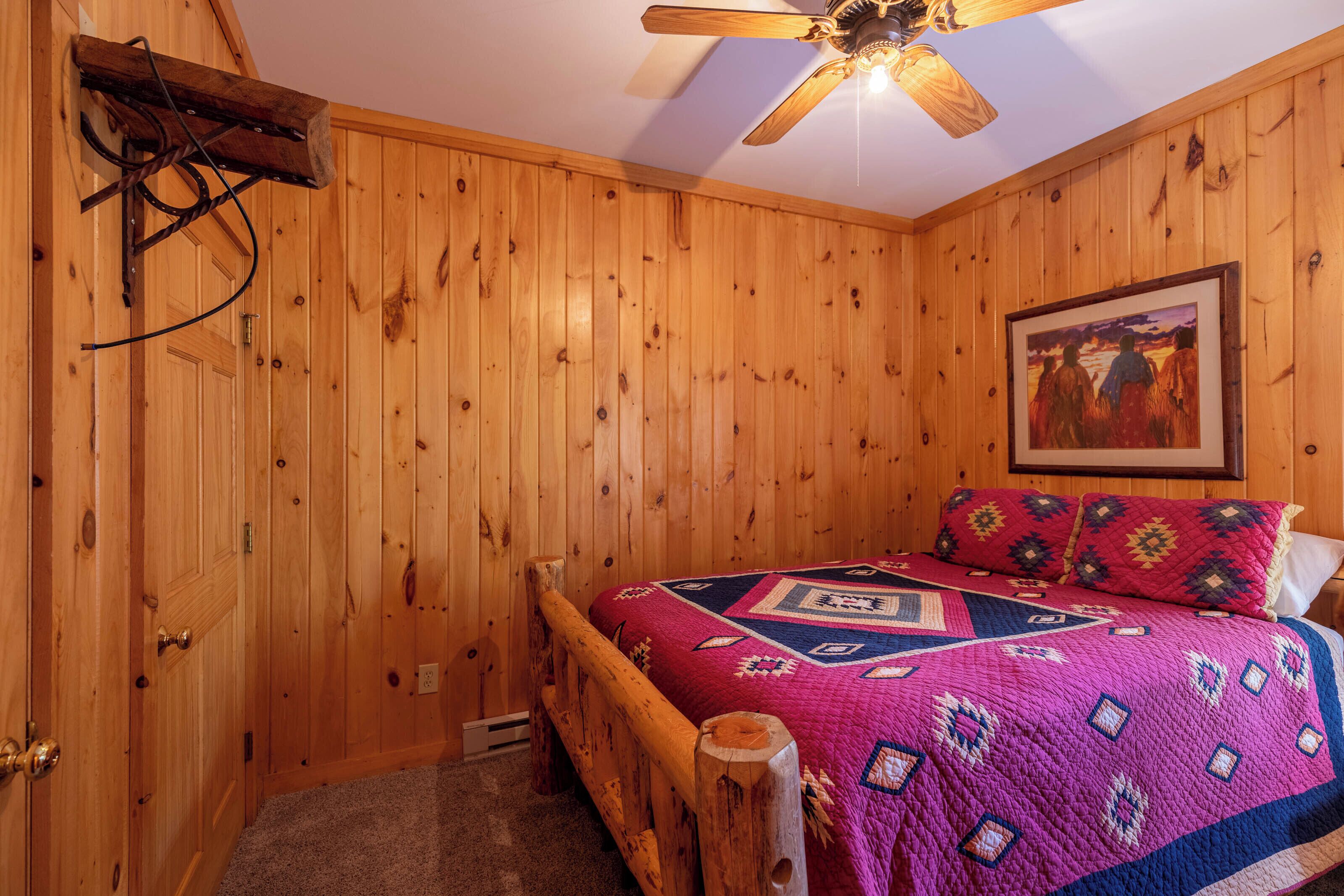 A wooden-paneled room with a bed, a ceiling fan, and a painting on the wall.
