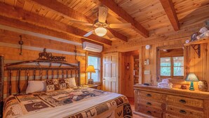 Een slaapkamer in een houten blokhut, met een bed, een dressoir en een plafondventilator.
