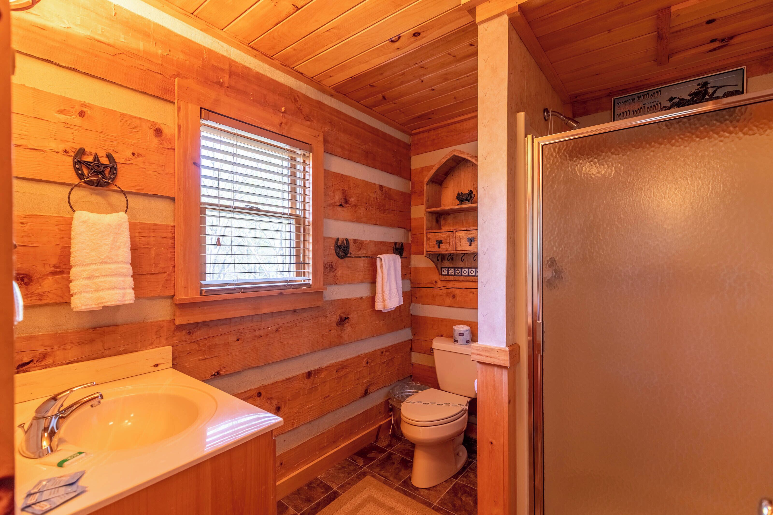 A wooden cabin bathroom with a sink, toilet, and window.