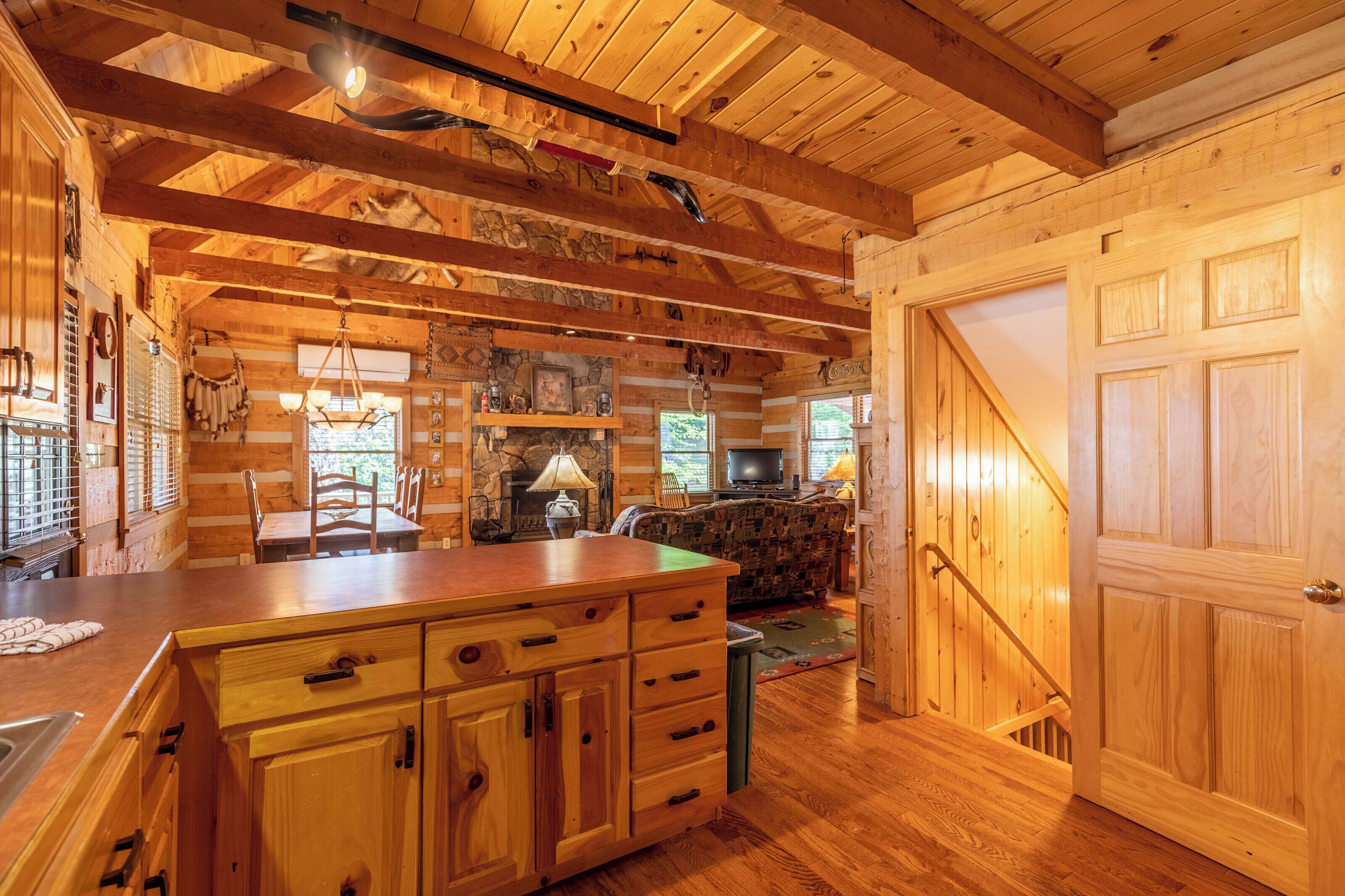 A log cabin interior with a wooden dining table, kitchen area, and a cozy fireplace.