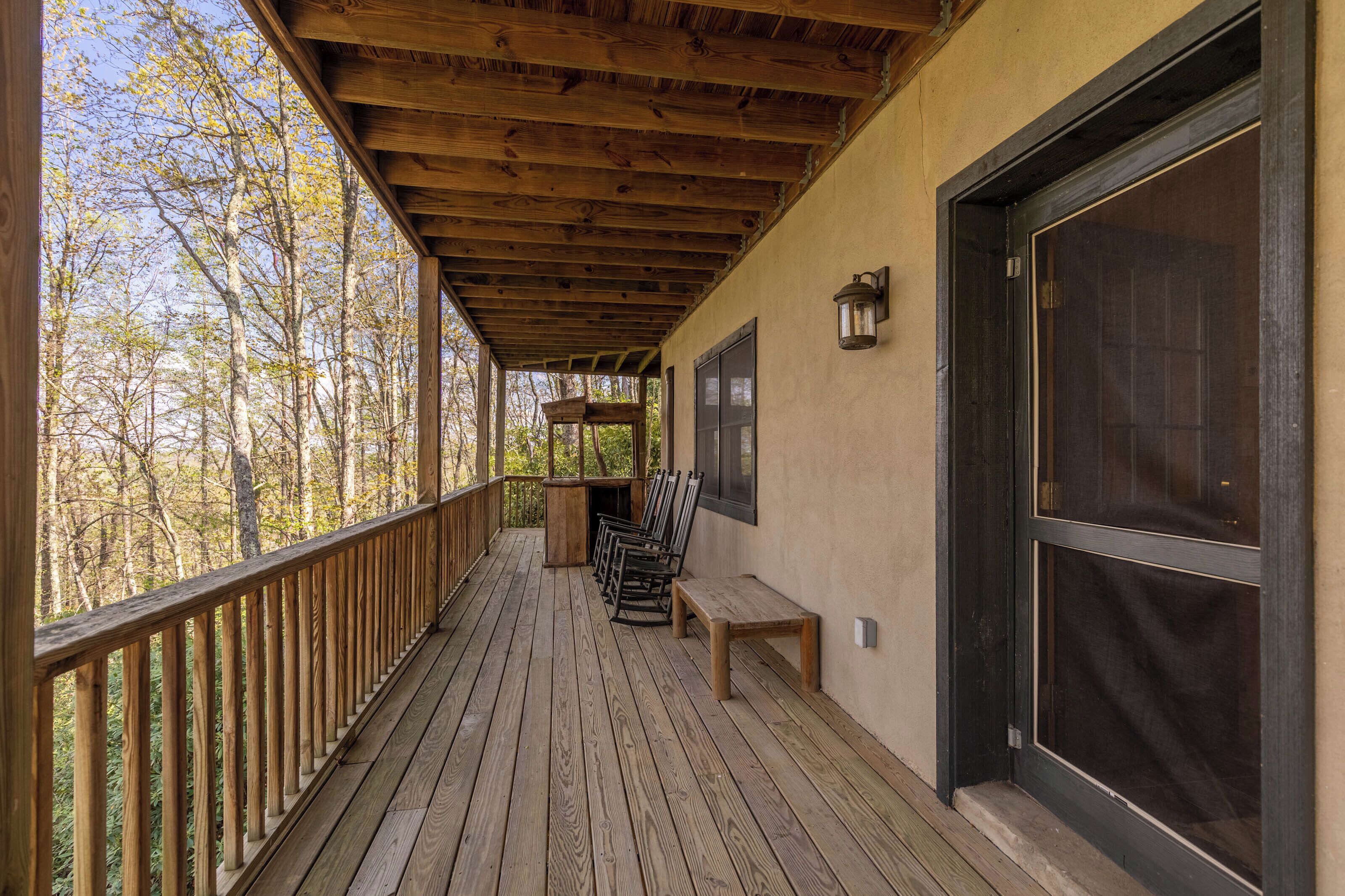 A wooden deck with a bench and chairs, overlooking a forested area.