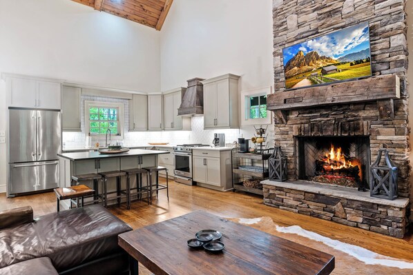 A spacious kitchen with a stone fireplace, a large island, and a modern stainless steel refrigerator.