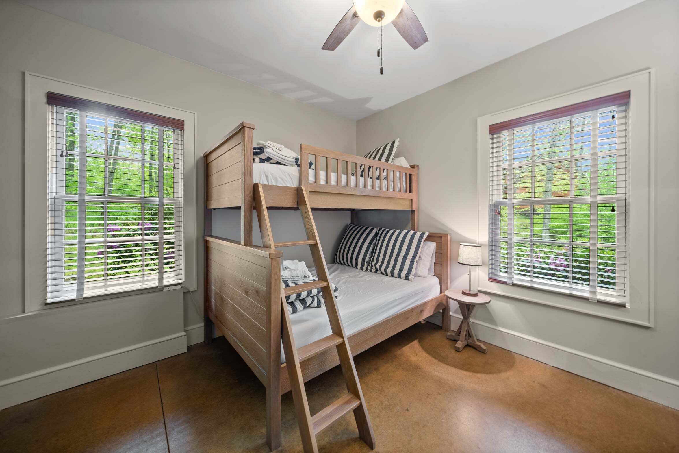 A bunk bed room with a ladder, a small bedside table, and a ceiling fan.