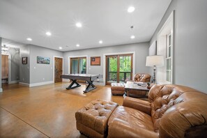 A spacious living room with a pool table, leather sofas, and a view of the outdoors. - Sweet Retreat at Sweetgrass (Blowing Rock)