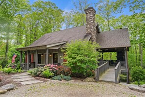 A lodge with a stone chimney, a covered porch, and a wooden deck.