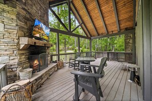 A covered outdoor deck with a stone fireplace, a television, and outdoor furniture.