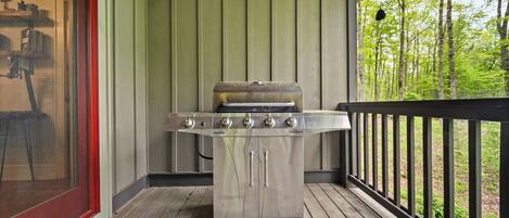 A stainless steel barbecue grill on a wooden deck with a view of a forest.