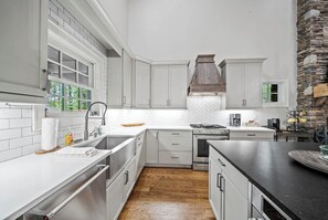 A kitchen with white cabinets, a stone accent wall, a wooden floor, and a black countertop.