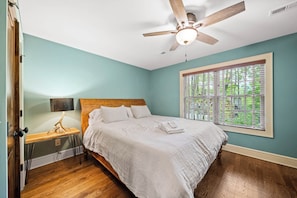 A bedroom with a bed, a ceiling fan, a window with blinds, and a wooden floor.