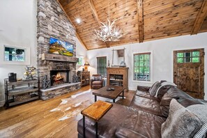 A cozy living room with a stone fireplace, leather sofa, and wooden ceiling beams.