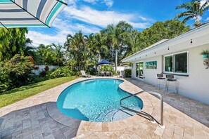 A swimming pool with a curved edge, surrounded by a patio area with chairs and a table.