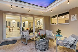 Une terrasse ensoleillée avec des portes-fenêtres coulissantes donnant sur un espace de vie, un coin salon extérieur et un panneau indiquant les règles à respecter au bord de la piscine.