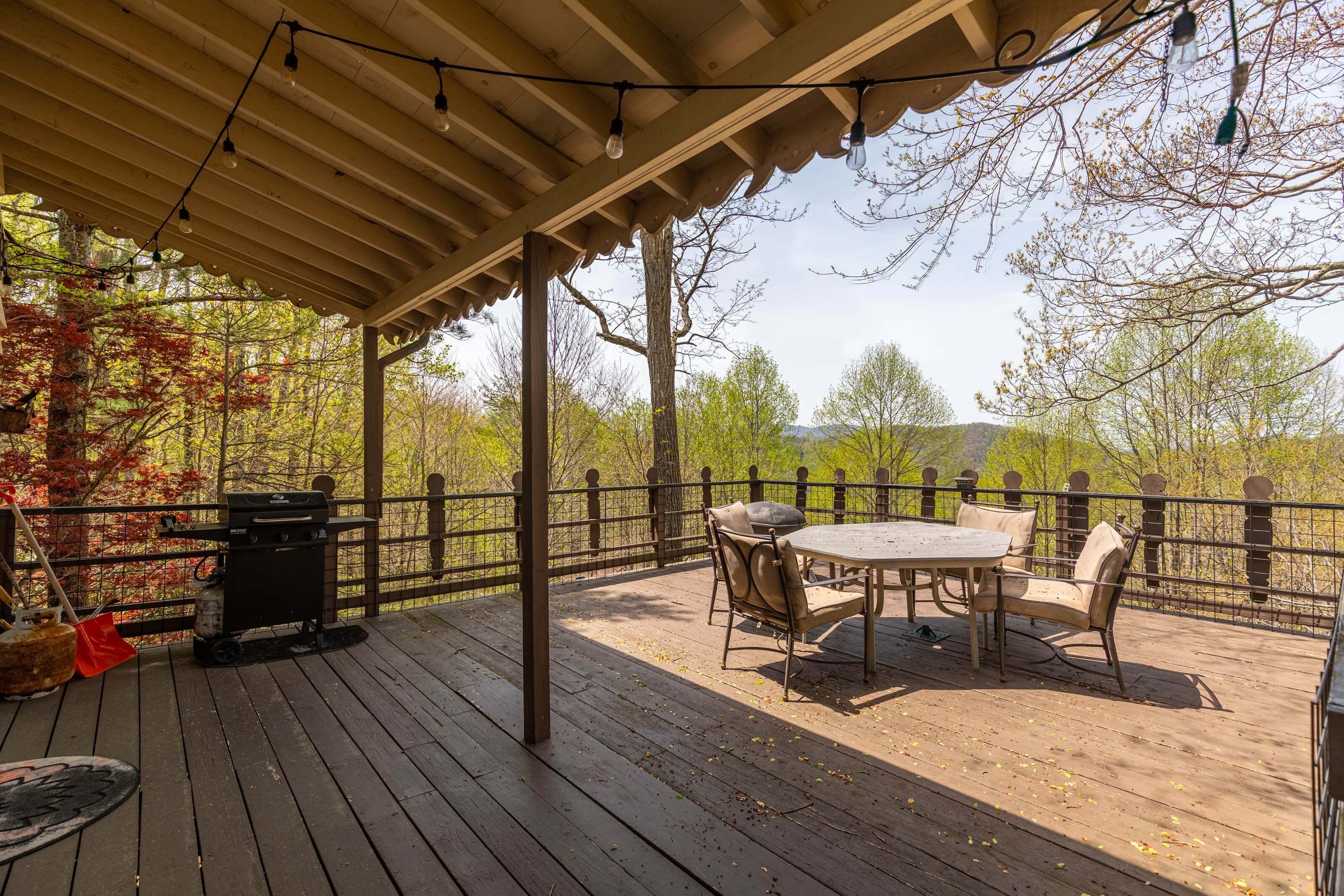 Une terrasse extérieure couverte, équipée d’un barbecue, d’une table et de chaises, et entourée d’une clôture en bois et d’arbres.