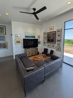 A modern living room with a sectional sofa, a coffee table, a flat-screen TV, and a ceiling fan.