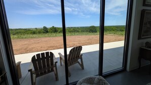 Una habitación con amplias ventanas que dan a un campo de tierra y vegetación, dos sillas de madera y una alfombra mullida.