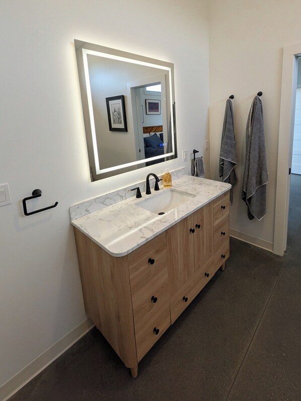 A bathroom with a large mirror, a sink, and wooden cabinets.
