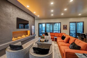 Ein modernes Wohnzimmer mit Kamin, einem orangefarbenen Sofa und einem großen Fenster mit Blick auf eine Terrasse.