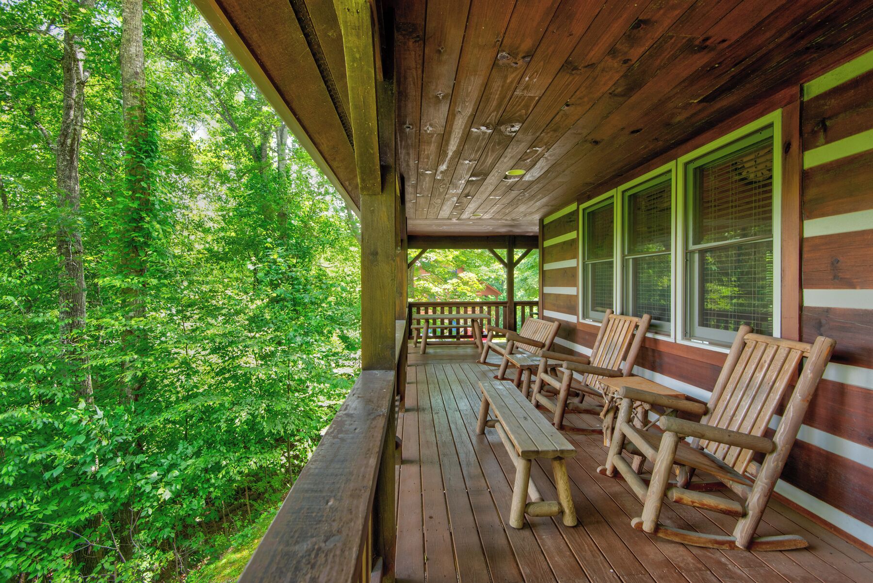 Une terrasse en bois, agrémentée de bancs et de fauteuils à bascule, entourée d’une végétation luxuriante.