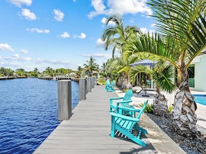 A wooden dock extending over a body of water with turquoise chairs and palm trees. - Bahama Breeze (Oakland Park)