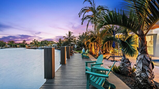 A wooden deck with chairs and a pool, surrounded by palm trees and a sunset sky. - Bahama Breeze (Oakland Park)