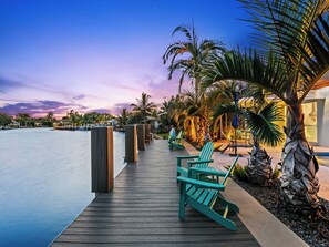 A wooden deck with chairs and a pool, surrounded by palm trees and a sunset sky. - Bahama Breeze (Oakland Park)