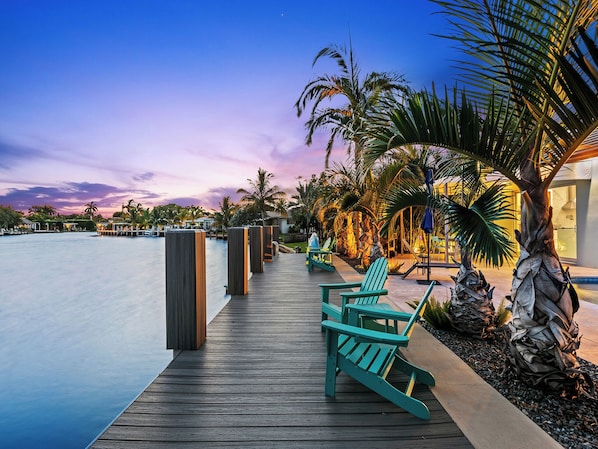 A wooden deck with chairs and a pool, surrounded by palm trees and a sunset sky. - Bahama Breeze (Oakland Park)