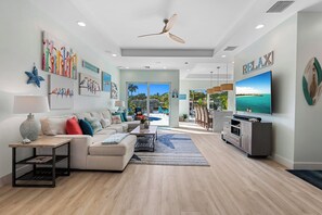 A spacious living room with a large TV, a ceiling fan, and artwork on the walls. - Bahama Breeze (Oakland Park)