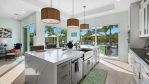 A modern kitchen with a large island, pendant lights, and a view of a pool and palm trees. - Bahama Breeze (Oakland Park)