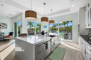 A modern kitchen with a large island, pendant lights, and a view of a pool and palm trees. - Bahama Breeze (Oakland Park)