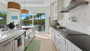 A modern kitchen with a large island, stainless steel appliances, and a view of a tropical outdoor area. - Bahama Breeze (Oakland Park)