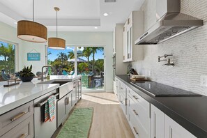 A modern kitchen with a large island, stainless steel appliances, and a view of a tropical outdoor area. - Bahama Breeze (Oakland Park)