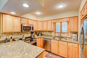 A modern kitchen with wooden cabinets, a granite countertop, stainless steel appliances, and a window with blinds.
