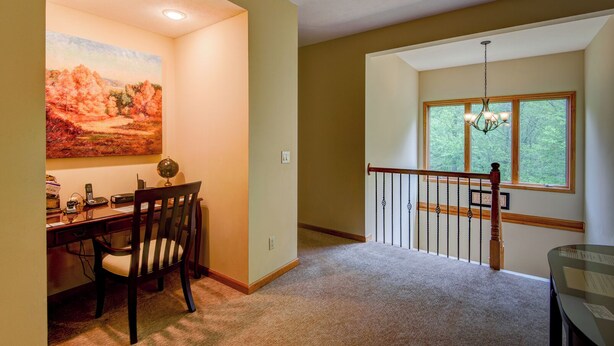 A dining area with a table and chairs, a painting on the wall, and a staircase leading to a balcony with a view of trees.