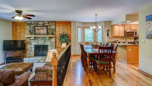 A spacious living area with a stone fireplace, wooden dining table, and a TV on a stand.