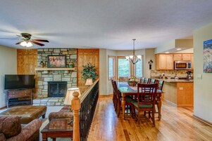 A spacious living area with a stone fireplace, wooden dining table, and a TV on a stand.