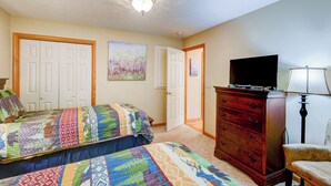 A bedroom with two beds, a dresser, a television, and a lamp.
