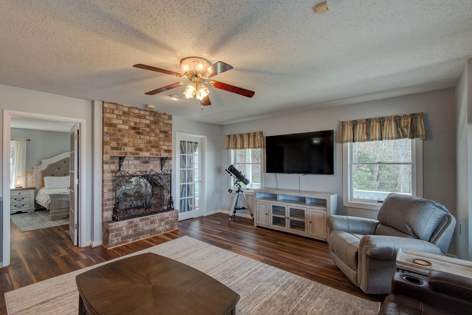 A spacious living room with a fireplace, a ceiling fan, a television, and a leather sofa.