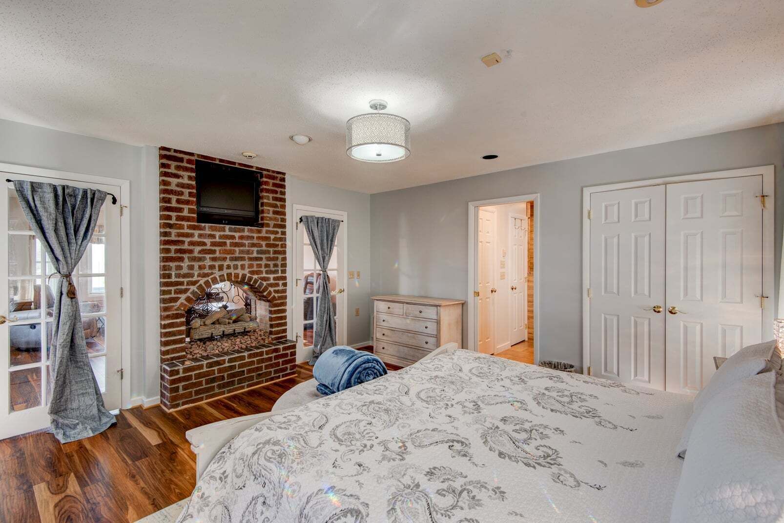 Une chambre avec une cheminée en briques, un lit avec une literie à motifs, une commode et une armoire.